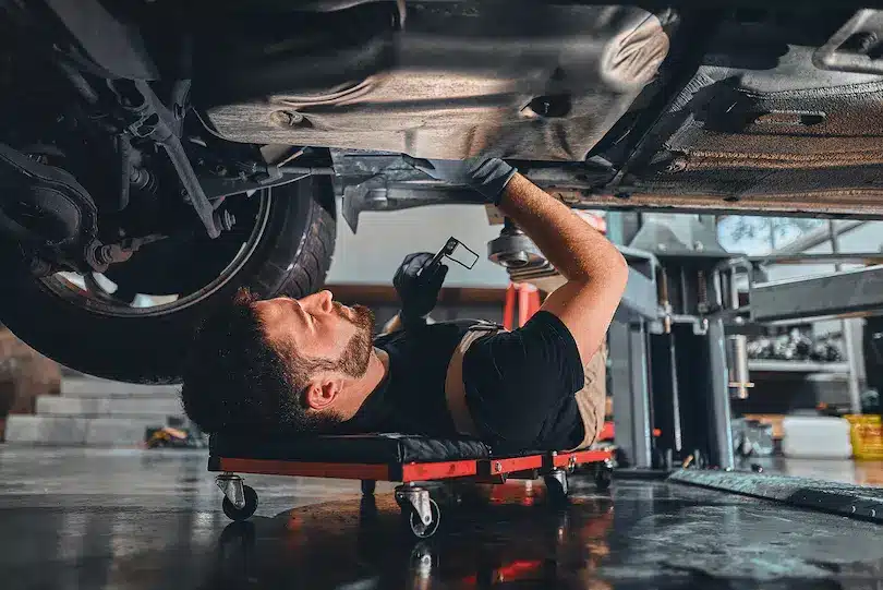 Careers, Auto repair shop in Springboro, OH, Springboro Automotive. Mechanic lying on a creeper under a car in a garage, using tools to work on the vehicles underside. The garage floor is clean, and thereβs a hydraulic lift nearby. The mechanic wears gloves and looks focused on the task.