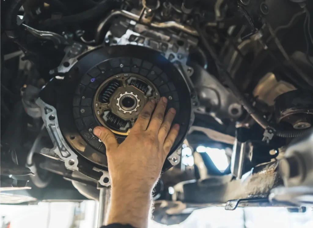 car maintenance near me, Auto repair shop in Springboro, OH, Springboro Automotive. A mechanics hand is inspecting a cars clutch system, focusing on the pressure plate and disc. The intricate mechanical parts are part of an exposed vehicle transmission system in a garage setting.