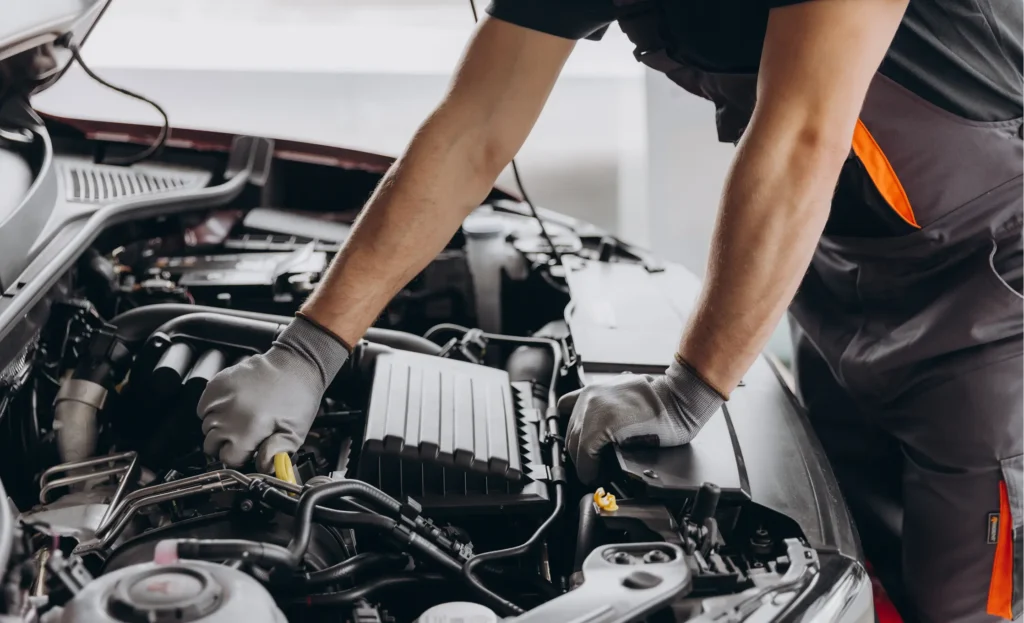 About us, Auto repair shop in Springboro, OH, Springboro Automotive. Mechanic wearing gloves works under the hood of a car, focusing on the engine area. Tools and car parts are visible, suggesting maintenance or repair work.