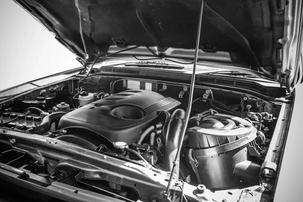 Diesel Repair, Auto repair shop in Springboro, OH, Springboro Automotive. Black and white image of a car engine under an open hood. Various components, including pipes, wires, and a large air filter, are visible. The engine parts are neatly arranged within the compartment.