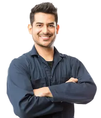 A smiling person in a dark blue work jumpsuit stands confidently with arms crossed against a plain background, embodying the professionalism of auto care services.