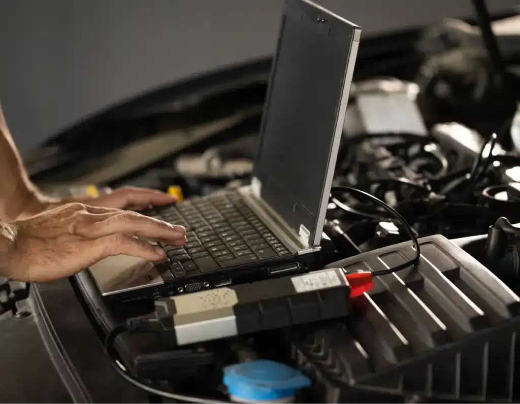 Asian auto repair, Auto repair shop in Springboro, OH, Springboro Automotive. Hands typing on a laptop placed on a car engine, with diagnostic cables connected.