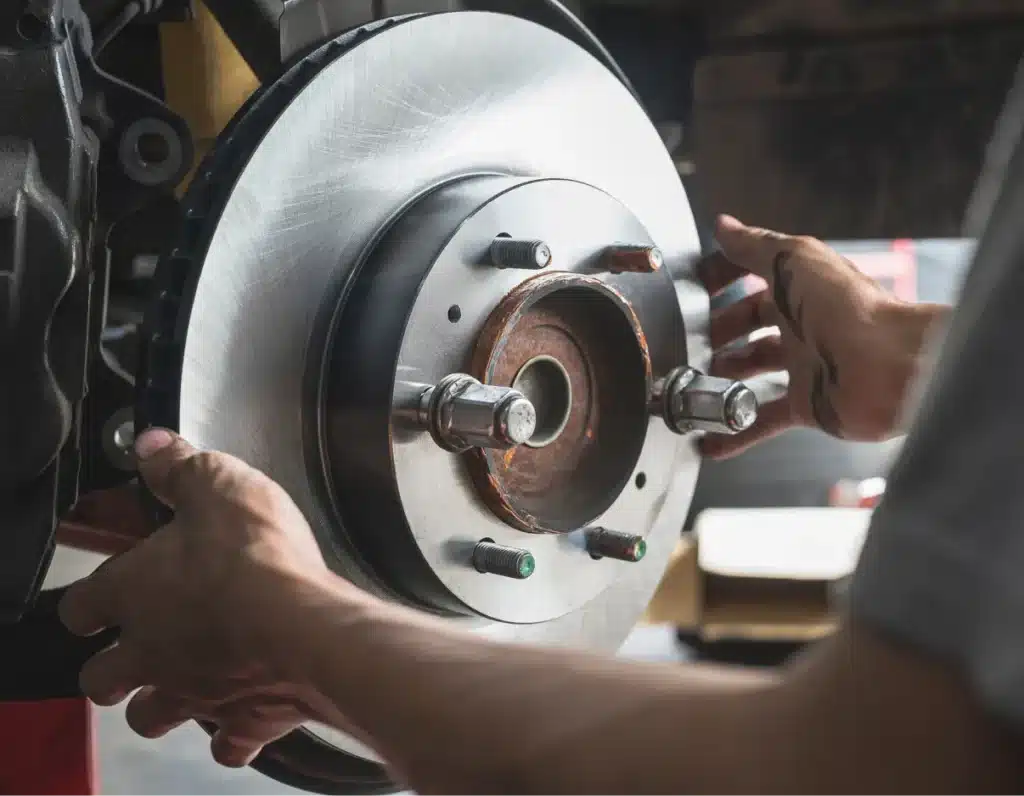 brake repair, Auto repair shop in Springboro, OH, Springboro Automotive. A person is installing a shiny, new brake disc onto a vehicles wheel hub. The persons hands are positioned on both sides of the disc, which is in focus while the background is blurred. The scene takes place in a garage or workshop.