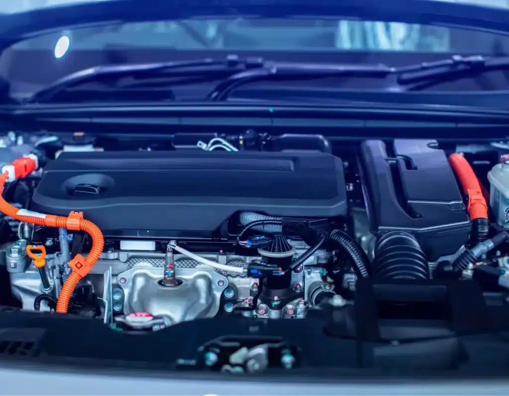 Hybrid car maintenance, Auto repair shop in Springboro, OH, Springboro Automotive. Close-up view of a car engine bay featuring various components, including pipes and cables. Bright orange wires are prominent, suggesting a hybrid or electric vehicle. The engine parts are neatly arranged under the hood.
