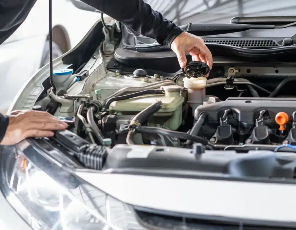 Vehicle inspection, Auto repair shop in Springboro, OH, Springboro Automotive. A person checking the fluid levels under the hood of a car, focusing on an open reservoir with the cap removed. The cars engine and various components are visible, with the person using one hand to hold the cap.