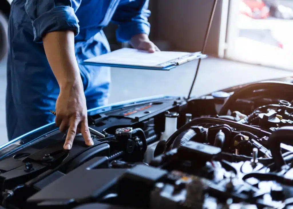 Vehicle inspection, Auto repair shop in Springboro, OH, Springboro Automotive. A mechanic in a blue jumpsuit inspects a car engine, holding a clipboard. The image focuses on the engine components and the mechanics hands, one pointing at a part. The setting is a well-lit garage or workshop.