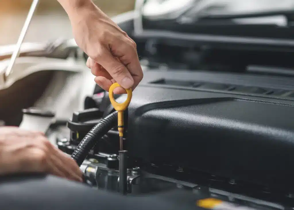 Auto care services, Auto repair shop in Springboro, OH, Springboro Automotive. A person checks a cars engine oil by pulling out the dipstick. The image focuses on the hand holding the yellow-ringed dipstick above the engine, with the vehicles hood open.