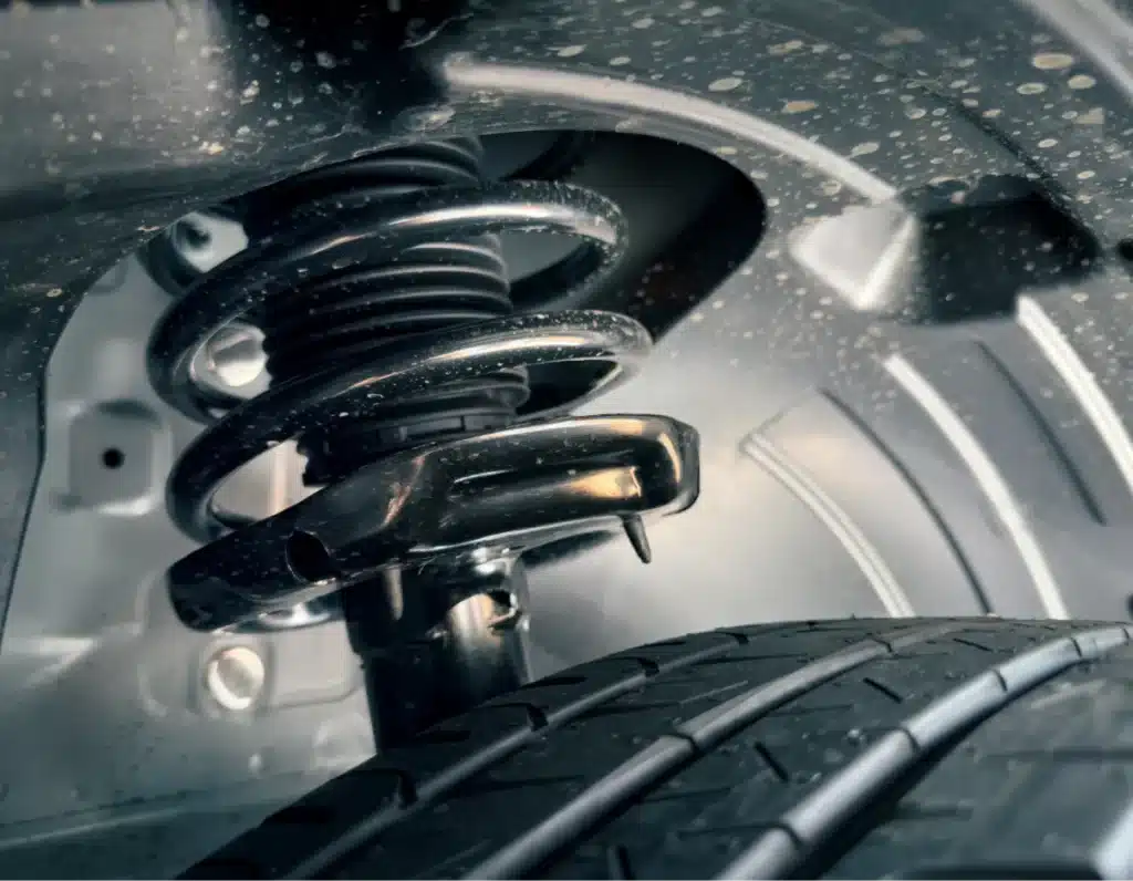 steering and suspension repair, Auto repair shop in Springboro, OH, Springboro Automotive. Close-up of a cars suspension system, showing the coil spring and associated components above a tire. The metal parts are new and shiny, with some dust and dirt visible. The tire tread is prominently displayed in the foreground.