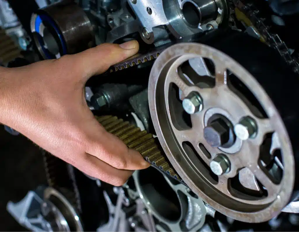 Timing belt replacement, Auto repair shop in Springboro, OH, Springboro Automotive. A person adjusts a timing belt on a car engine. The engine components include gears and bolts, and the persons hand is visible, focusing on the belt. The scene is well-lit, highlighting the mechanical details.