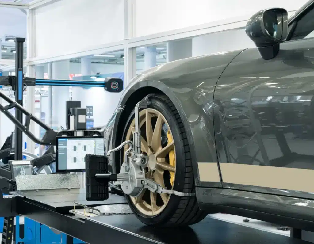 wheel alignment, Auto repair shop in Springboro, OH, Springboro Automotive. A car is on an alignment platform in a garage. The side of the car is visible with a focus on the front wheel, which is clamped with alignment equipment. A monitor is displaying data beside the car.