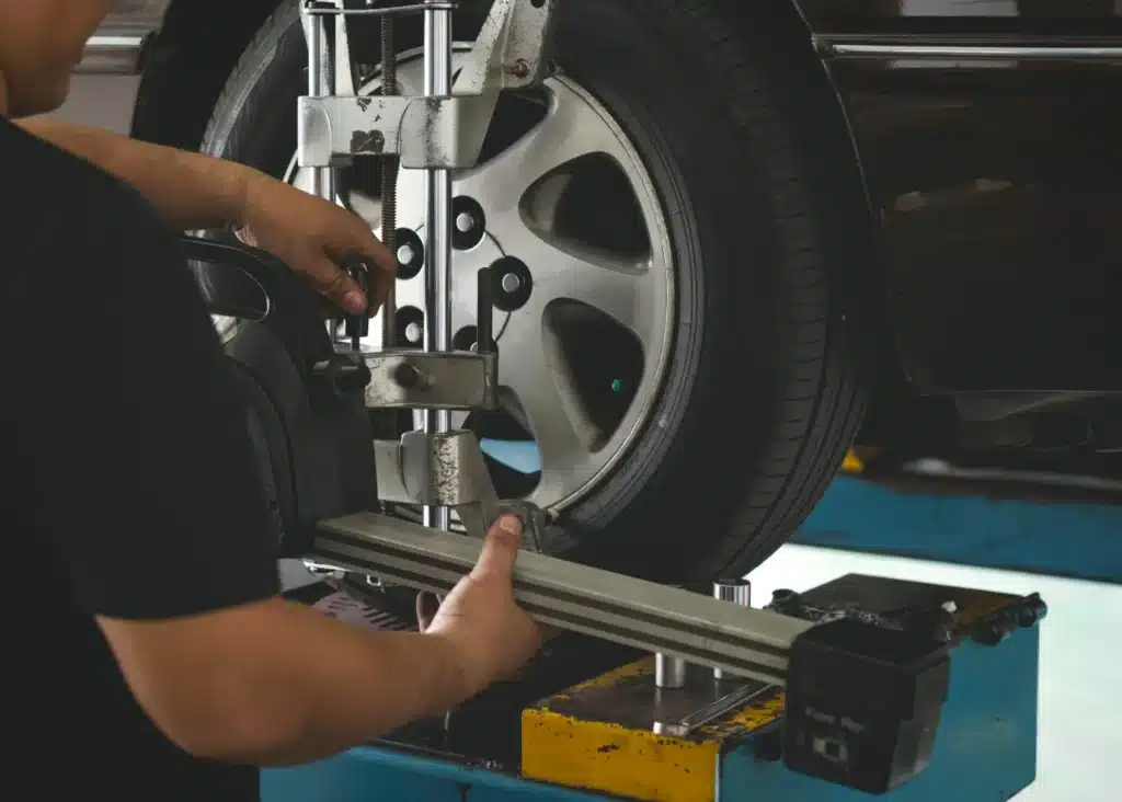wheel alignment, Auto repair shop in Springboro, OH, Springboro Automotive. A mechanic is adjusting the alignment of a cars tire on a hydraulic lift. They are using a specialized tool attached to the wheel. The cars metallic alloy wheel and part of its body are visible.