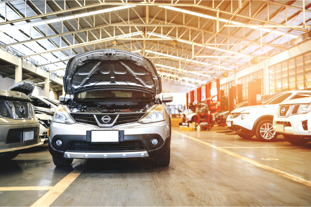 Car Maintenance. Auto repair in Springboro, OH. Springboro Automotive. A silver Nissan car with its hood open inside a well-lit automotive service center, surrounded by other vehicles and repair bays.